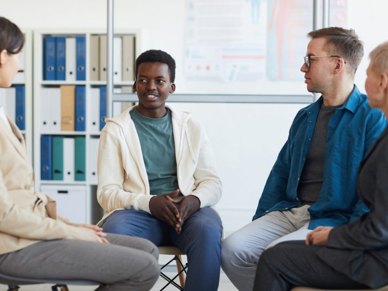 Portrait of young African-American man sitting on chair in support group circle and sharing story